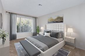 Danville apartment for rent - A carpeted  bedroom features a large bed with gray accents, nightstands with lamps, a large window with vertical blinds.