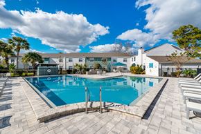 Casselberry townhouse for rent - A large outdoor swimming pool surrounded by lounge chairs and a building in the background.