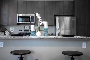Loveland apartment for rent - A kitchen with a stainless steel refrigerator and a microwave above a counter with two black stools.