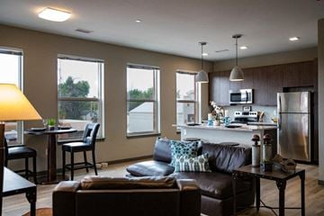 Loveland apartment for rent - A modern living room with a brown leather couch and a kitchen area in the background.