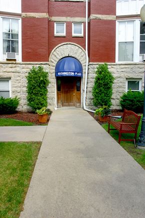Appleton apartment for rent - a walkway in front of a brick building with a blue sign on the door