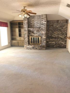 Abilene house for rent - an empty living room with a fireplace and a ceiling fan