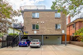 Denver apartment for rent - Two cars are parked in a garage in front of a brick building.