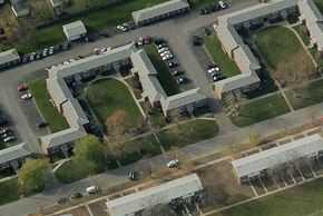 Tonawanda apartment for rent - A parking lot is surrounded by a building with a grassy area in the middle.