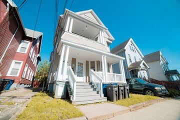New Haven apartment for rent - A white two-story house with a porch and a car parked in front.