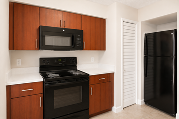 Deerfield Beach apartment for rent - A black microwave is mounted above a black stove in a kitchen with wooden cabinets.