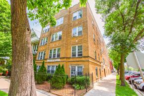 Chicago apartment for rent - A red brick building with a black fence and green trees in front.