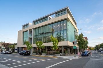 Palo Alto apartment for rent - A modern building with glass windows and a sign that reads "magso" is situated on a street corner with cars parked in front.