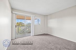 Santa Ana townhouse for rent - A room with a carpeted floor and a view of the beach through a sliding glass door.