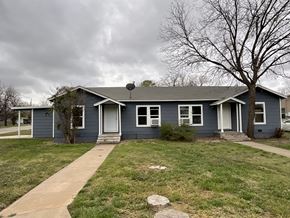Abilene apartment for rent - A house with a grey roof and white door is surrounded by a grassy lawn.