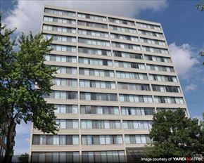 Chicago apartment for rent - A tall building with many windows is surrounded by trees.