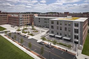 Lowell apartment for rent - A modern building with a green roof is surrounded by other buildings.