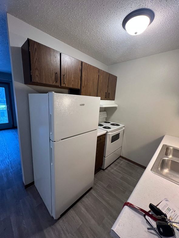 Moorhead apartment for rent - A white refrigerator is in a kitchen with a sink and wooden cabinets.