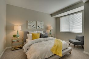 Eagan apartment for rent - Bed with white comforter and different colored pillows, endtables with lamps, and a gray chair in the corner by the window