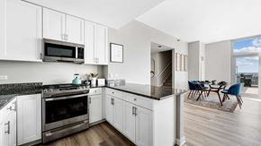 Chicago apartment for rent - Standing in a kitchen in a residence at Burnham Pointe. The oven and microwave are seen on the left with white cabinets all around. A counter is in the middle separating the kitchen from the dining.