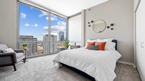 Chicago apartment for rent - A bedroom in a residence at Burnham Pointe. A large bed is set on the right with floor-to-ceiling windows on the left showing the city outside.