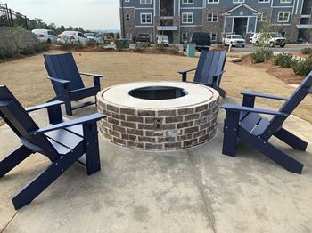 A fire pit surrounded by blue chairs in a concrete patio area.