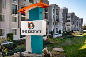 La Mesa apartment for rent - One-Bedroom Apartments in La Mesa, CA - The District - A Modern Apartment Community Exterior with a Large Property Entrance Sign and Landscaped Greenery.
