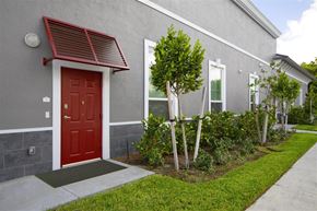 Miami apartment for rent - a red door on a gray building with a sidewalk and plants
