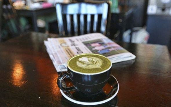 New Orleans apartment for rent - A cup of coffee with latte art on top sits on a saucer with a newspaper and a chair in the background.
