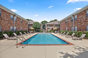 Metairie apartment for rent - A swimming pool surrounded by lounge chairs in front of a brick building.