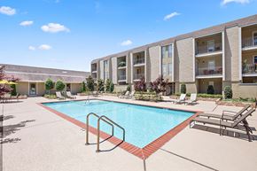 Metairie apartment for rent - A swimming pool surrounded by lounge chairs and apartment buildings.