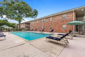 Metairie apartment for rent - A pool area with sun loungers and a brick building in the background.