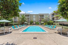 Metairie apartment for rent - A swimming pool surrounded by lounge chairs and umbrellas in front of apartment buildings.