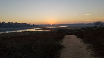 Huntington Beach house for rent - A path leads through a field towards a body of water with the sun setting in the distance.