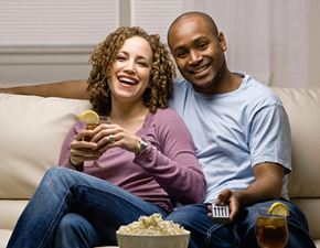 Fort Lee apartment for rent - A couple is sitting on a couch, eating popcorn and drinking beverages while watching television.