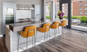 Chicago apartment for rent - Orange bar chairs site before the bar and commercial kitchen in the rooftop club. A large cooktop is seen behind the bar.