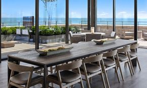 Chicago apartment for rent - A long dinging room table sits in a open room with floor-to-celing windows. The sky terrace is seen outside and Lake Michigan beyond on a sunny day.