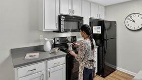 San Marcos apartment for rent - A woman is cooking in a kitchen with a black refrigerator and a clock on the wall.