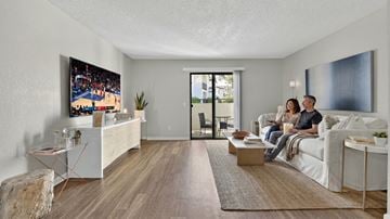 San Marcos apartment for rent - A couple is sitting on a couch in a living room with a television playing basketball.
