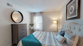 Greensboro apartment for rent - A bedroom with a bed, nightstand, lamp, and a mirror on the wall.