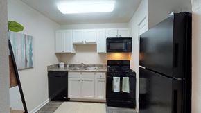Greensboro apartment for rent - A black refrigerator sits in a kitchen with white cabinets.