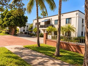 Miami apartment for rent - A white building with a red brick wall and palm trees in front.