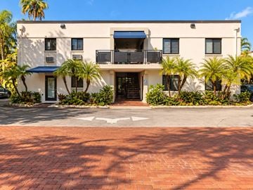 Miami apartment for rent - A white building with a balcony and palm trees in front.
