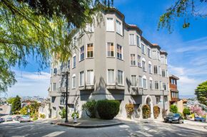 San Francisco apartment for rent - A large grey building with a curved corner and a tree in front of it.