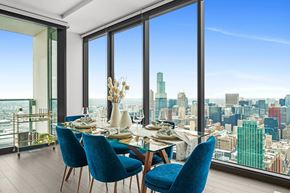 Chicago apartment for rent - A dining room with blue chairs and a table set for a meal with a city view.