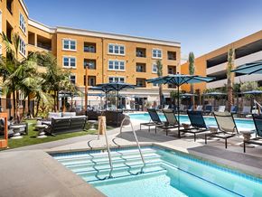 Anaheim apartment for rent - A pool area with lounge chairs and umbrellas in front of a multi-story building.