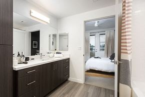 Anaheim apartment for rent - A bedroom with a large mirror, a vanity with a sink, and a bed with a white comforter.