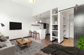 Denver apartment for rent - A living room with a grey couch, a coffee table, a television, and a kitchen area in the background.