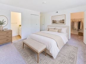 Levittown apartment for rent - A bedroom with a large bed, a bench, and a clothing rack.