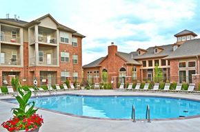 Omaha apartment for rent - A large swimming pool in front of a brick building with a red roof.