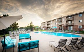 Sioux City apartment for rent - a swimming pool with blue chairs and umbrellas in front of an apartment building