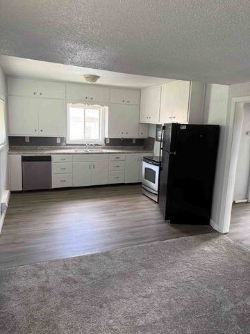 Fargo apartment for rent - A black refrigerator stands in a kitchen with white cabinets and a wooden floor.