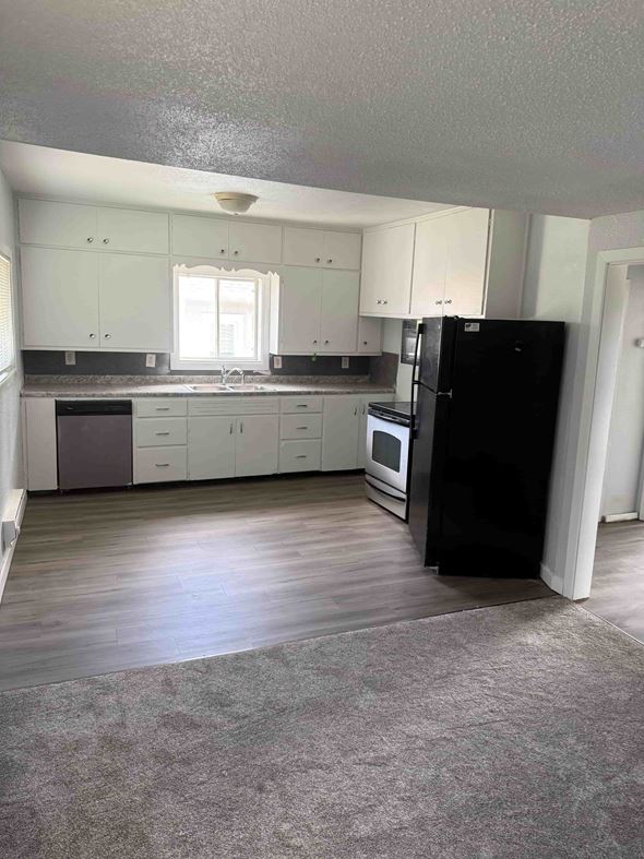 Fargo apartment for rent - A black refrigerator stands in a kitchen with white cabinets and a wooden floor.