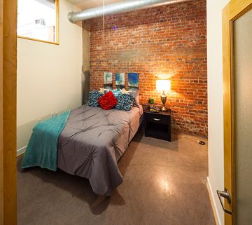 Richmond apartment for rent - A bedroom with a brick wall and a bed with a teal blanket.