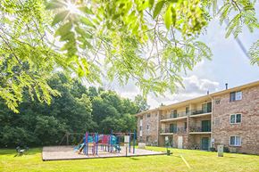 Beech Grove apartment for rent - A playground with a slide and swings is surrounded by trees and a building.
